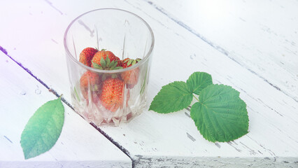 strawberries in a glass on a white wooden table. the concept of summer holidays at grandma's