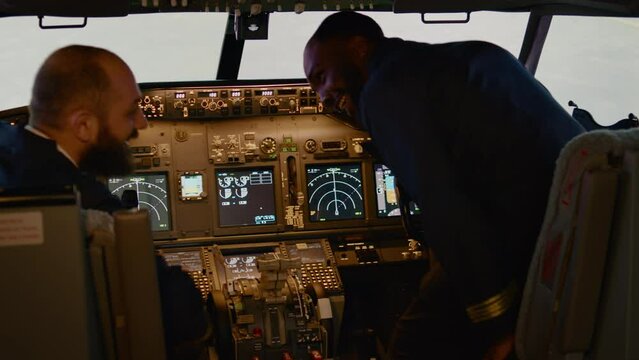 Diverse team of captain and copilot preparing to takeoff with airplane, inserting destination coordinates in cockpit control panel. Aircrew flying plane using dashboard command. Handheld shot.