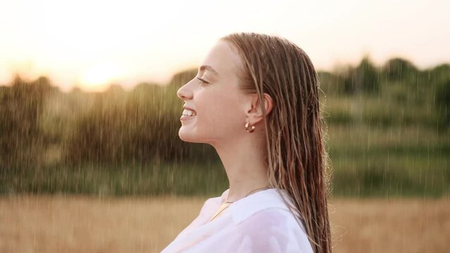 Gorgeous girl under rain with beautiful sunset. Golden sun rays shine on attractive  young woman enjoying a summer rain.