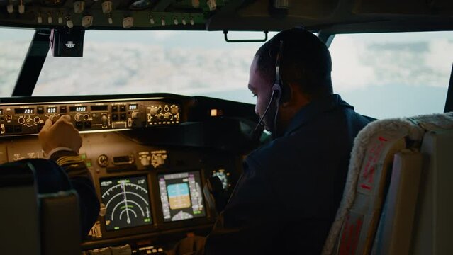 African american copilot flying airplane with captain in cockpit, throttling engine handle and fixing altitude and longitude. Navigation command on dashboard and control panel. Handheld shot.