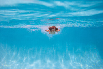 Young boy swim and dive underwater. Under water portrait in swim pool. Child boy diving into a...