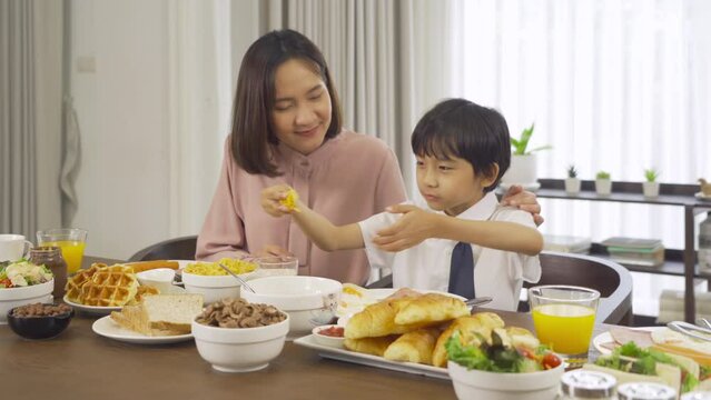 Portrait of happy smiling Asian Family eating breakfast food together before the child going to school at home. Family relationship. Love of mother, and son. People lifestyle.