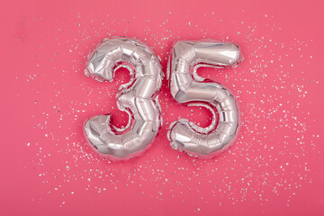 Silver balloon number 35 thirty five shape sparkles scattered randomly on juicy pink background....