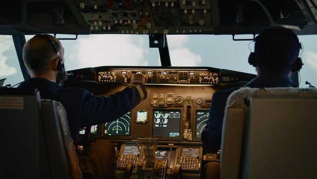 Diverse team of captain and copilot using dashboard command to takeoff and fly airplane. Pushing buttons to switch altitude and longitude on control panel in cockpit. Handheld shot.