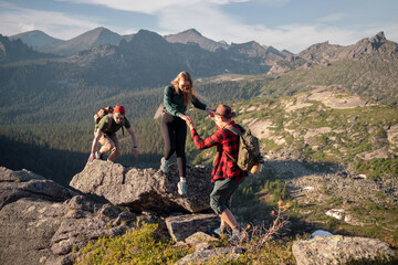 Fototapeta premium Group of young tourists two guys and girl with backpacks in mountains go along route