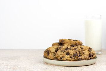 A stack of chocolate chip cookies on a white plate with a glass of milk on a white background. Selective focus. Copy space.