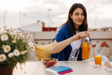 Pretty young caucasian woman is looking at camera, sitting at juice table in open air. Brunette...