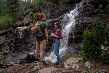 Young tourists adventurers girl and guy on background of waterfall in forest