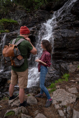 Young tourists adventurers girl and guy on background of waterfall in forest