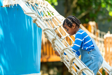 Happy Little African child boy playing and climbing rope net at outdoor playground in the park on...
