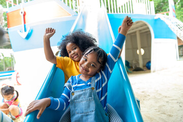 Happy Little African child boy and girl friends sliding and playing at outdoor playground in the...