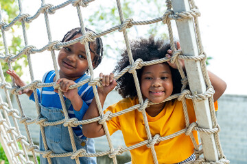 Little African boy and girl friends playing and climbing rope net together at playground in the...