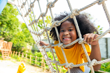 Happy Little African child girl playing and climbing rope net at outdoor playground in the park on...