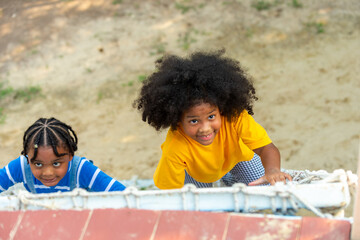 Little African boy and girl friends playing and climbing rope net together at playground in the...