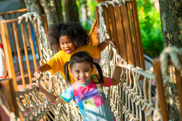 Group of Happy Little boy and girl friends playing and climbing rope net together at playground park on summer vacation. Children kid enjoy outdoor activity playing and learning at school playground