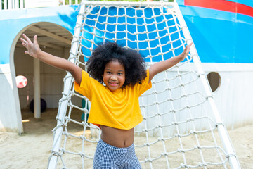 Happy Little African child girl playing and climbing rope net at outdoor playground in the park on...