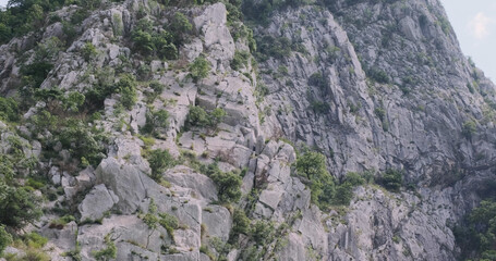 Mountain gray rocks covered green bushes in summer on sunny day. Travel through Albania mountains. Beautiful view of stone mountains. Flying around Rocky, strong mountains rise. Balkan Peninsula