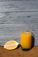 A composition of fresh fruit and drink, lemon around an orange juice in a glass, on a dark textured...