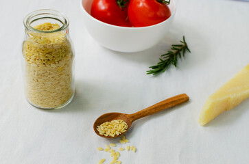 Raw Italian risoni pasta in a glass jar with ingredients on a table. The concept of traditional cuisine. Horizontal orientation.