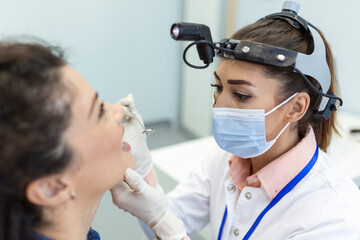 Female patient opening her mouth for the doctor to look in her throat. Otolaryngologist examines sore throat of patient.