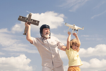 Child boy and grandfather hold plane and drone quad copter against sky. Child pilot aviator with plane dreams of flying.