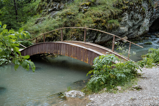 Equipped pedestrian crossing over the river wooden bridge, a bridge in the form of an arch thrown over a mountain stream, an ecological trail in the park, hiking in the forest.