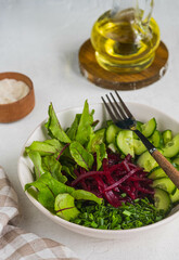 Vegetable salad with beetroot leaves, cucumber, green onions and pickled beets, dressed with olive oil, in a ceramic bowl on a light concrete background. Vegan Recipes.