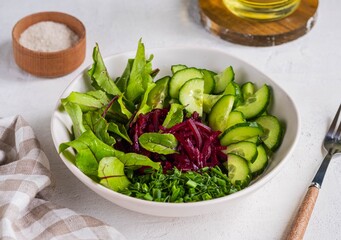 Vegetable salad with beetroot leaves, cucumber, green onions and pickled beets, dressed with olive oil, in a ceramic bowl on a light concrete background. Vegan Recipes. Healthy food