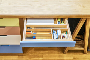 Obraz na płótnie Canvas Sawhorse desk with cabinet and multi-colored roll-out drawers with stationery. Fragment of furniture made of plywood and solid oak upper angle view