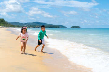 Happy Asian family on beach vacation. Little child boy and girl sibling playing sea water at the beach in summer sunny day. Children kid enjoy and fun outdoor activity lifestyle together at the sea