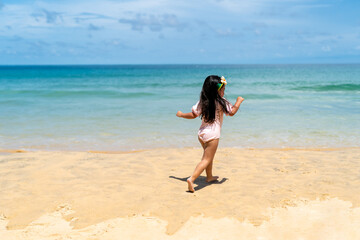Happy Asian little child girl in swimwear running and playing on tropical beach in summer sunny day. Children kid enjoy and fun outdoor activity lifestyle travel vacation on beach holiday at the sea