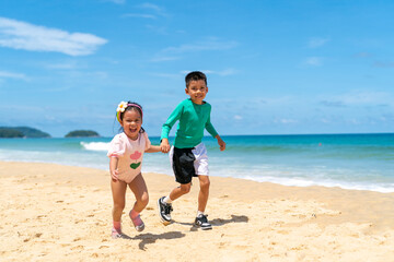 Happy Asian family on beach vacation. Little child boy and girl sibling playing sea water at the beach in summer sunny day. Children kid enjoy and fun outdoor activity lifestyle together at the sea