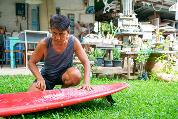 Healthy Asian senior man waxing surfboard surface at home. Active elderly male surfer enjoy outdoor...
