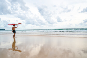 Healthy Asian senior man surfer in swimwear holding surfboard walking on the beach at summer...