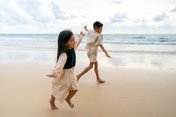 Happy Asian family on summer beach vacation. Little child boy and girl sibling playing together on the beach at summer sunset. Children kid enjoy and fun outdoor activity lifestyle playing at the sea