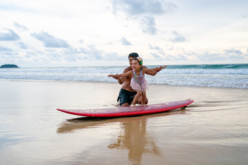 Happy Asian family grandfather teaching little grandchild girl surfing on surfboard at the beach....