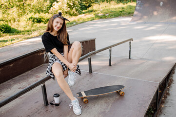 Stylish teenager girl with skateboard sitting and chilling in the skaters park