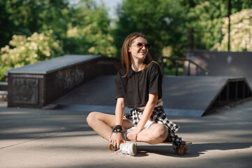 Stylish teenager girl with skateboard sitting and chilling in the skaters park