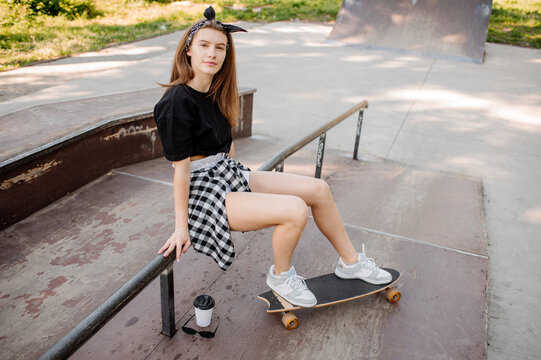 Stylish teenager girl with skateboard sitting and chilling in the skaters park
