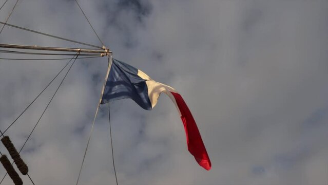 Drapeau fran&ccedil;ais accroch&eacute; &agrave; un m&acirc;t de bateau flottant dans le vent au coucher du soleil