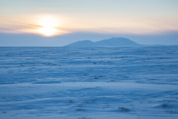 Fototapeta na wymiar Winter arctic landscape. View of the snow-covered tundra and snow-capped mountains. Cold frosty winter weather. Endless Arctic Desert. Northern nature of the polar region. Sunset. Chukotka, Russia.