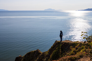 A woman stands near a cliff on the sea coast. Beautiful seascape. A woman looks at the sea from the shore. Travel and tourism in the Russian Far East. Sea of Okhotsk, Magadan region, Russia. Autumn.