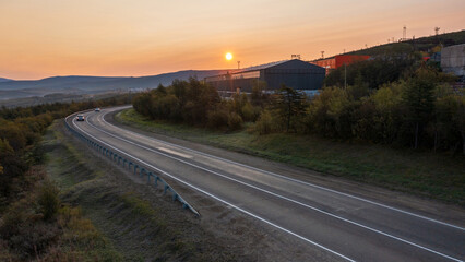 Morning aerial view of a highway. Sunrise over asphalt road and industrial buildings. Beautiful landscape. Road trip across Siberia. Kolyma highway, Magadan region, Far East of Russia.