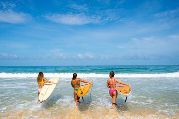  Group of Asian woman surfer in swimwear holding surfboard walking together on tropical beach in sunny day. Female friends enjoy outdoor activity lifestyle water sport surfing on summer vacation - obrazy, fototapety, plakaty