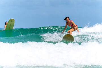 Asian woman surfer surfing and riding surfboard  the wave in the sea at tropical beach in sunny...
