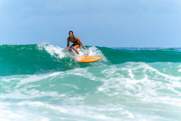 Asian woman surfer surfing and riding surfboard  the wave in the sea at tropical beach in sunny...