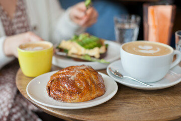 breakfast at bakery with a freshly baked cinnamon bun and eggs and avocado toast. Cup of specialty coffee at cafe. Brunch with friends. Candid lifestyle.