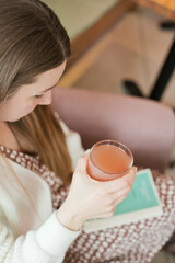 Woman reading a book at cafe and drinking juice or cocktail. Candid cafe lifestyle. Turning pages in the book. Stylish woman at coffee house. Real woman in restaurant.