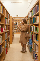 Young woman at the library holding book. millennial reading books, standing between bookshelves in...