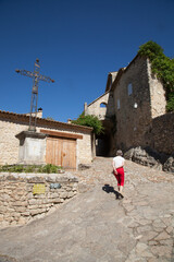 Touriste femme montant une ruelle du village touristique de la Roque sur Cèze et passant au pied d'une croix métallique